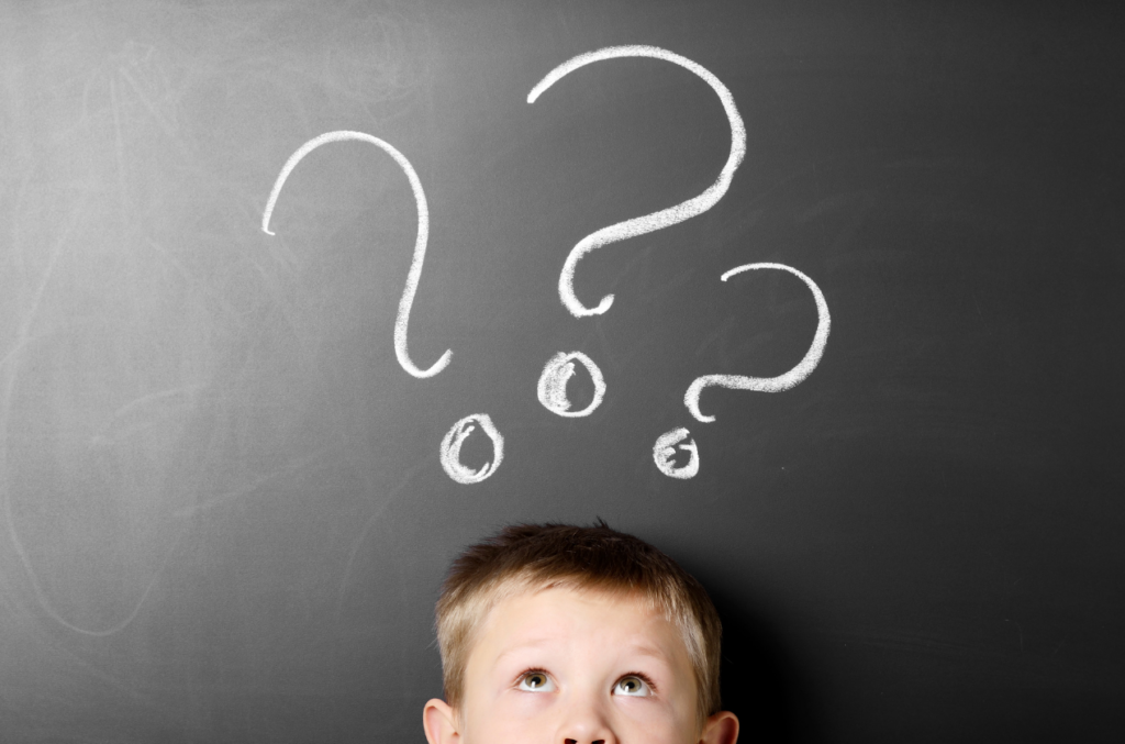 young boy standing under three chalk question marks