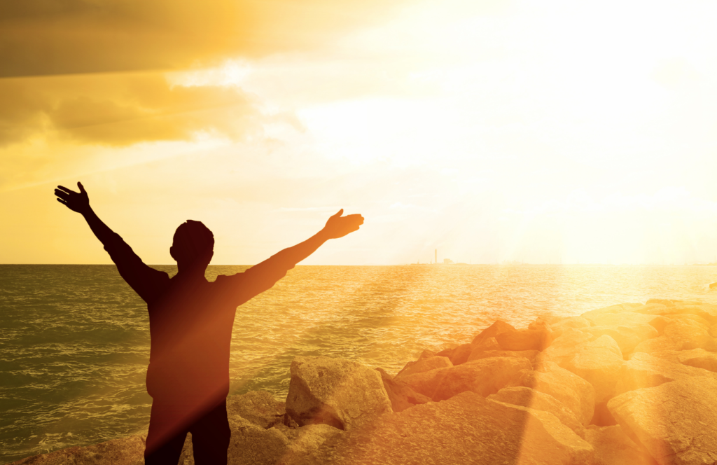 person rejoicing in front of water in the rays of the sun